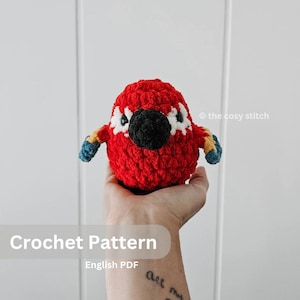 May include: Crochet pattern for a red, black, and blue parrot amigurumi toy. The pattern is available as an English PDF download.  © the cosy stitch