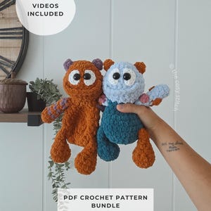 Op de afbeelding: Twee gehaakte pluche monsterknuffels, één in roestoranje en één in lichtblauw met donkergroene benen, voorzien van grote witte ogen met zwarte pupillen, kleine oren en getextureerd garen. Tekst: HELPFUL VIDEOS INCLUDED en PDF CROCHET PATTERN BUNDLE.