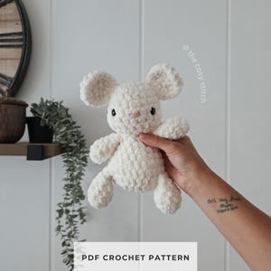 Puede incluir: Un pequeño juguete de ratón de ganchillo de felpa color blanco roto con orejas redondas, ojos de cuentas negras y una pequeña nariz rosa. El texto "the cosy stitch" es visible arriba a la derecha y "PDF CROCHET PATTERN" está centrado abajo.