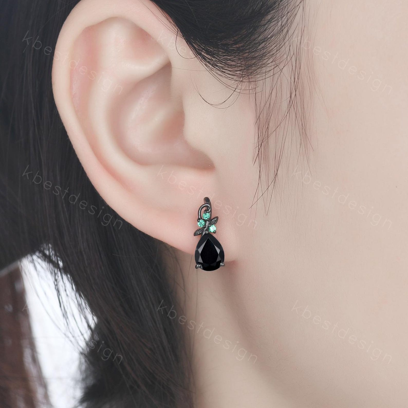 Woman wearing black onyx and emerald stud earrings with black hair tucked behind ear
