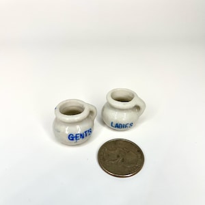 May include: Two small white ceramic jugs with blue lettering. One jug says "GENT'S" and the other says "LADIES".