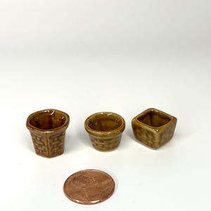 May include: Three small brown ceramic planters, one round, one square, and one hexagonal, with a woven pattern. A penny is included for scale.