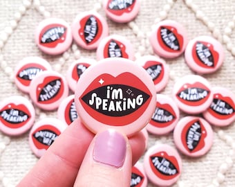May include: A close-up of a pink button with a red mouth and the text "i'm speaking" in black. The button is being held by a hand.