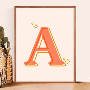 May include: A framed print with a stylized orange and pink letter A with a yellow outline. The letter is surrounded by small yellow stars.