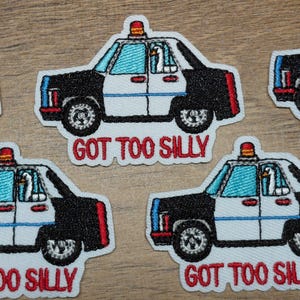 May include: Embroidered patches featuring a black and white police car design with a duck inside. The patches have the text "GOT TOO SILLY" in red. Each patch has a red and orange light on top.