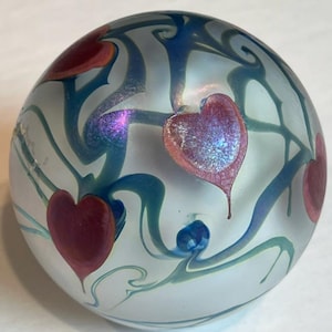 May include: A white glass paperweight with blue and green swirls and four pink hearts.