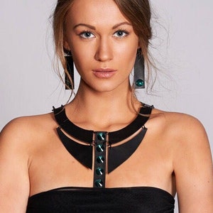 Puede incluir: Una mujer con un vestido negro sin tirantes y un collar geométrico negro y verde. El collar tiene un diseño grande y abierto con una serie de piedras preciosas verdes.