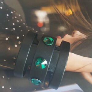May include: A black leather bracelet with three straps and three green crystal embellishments.