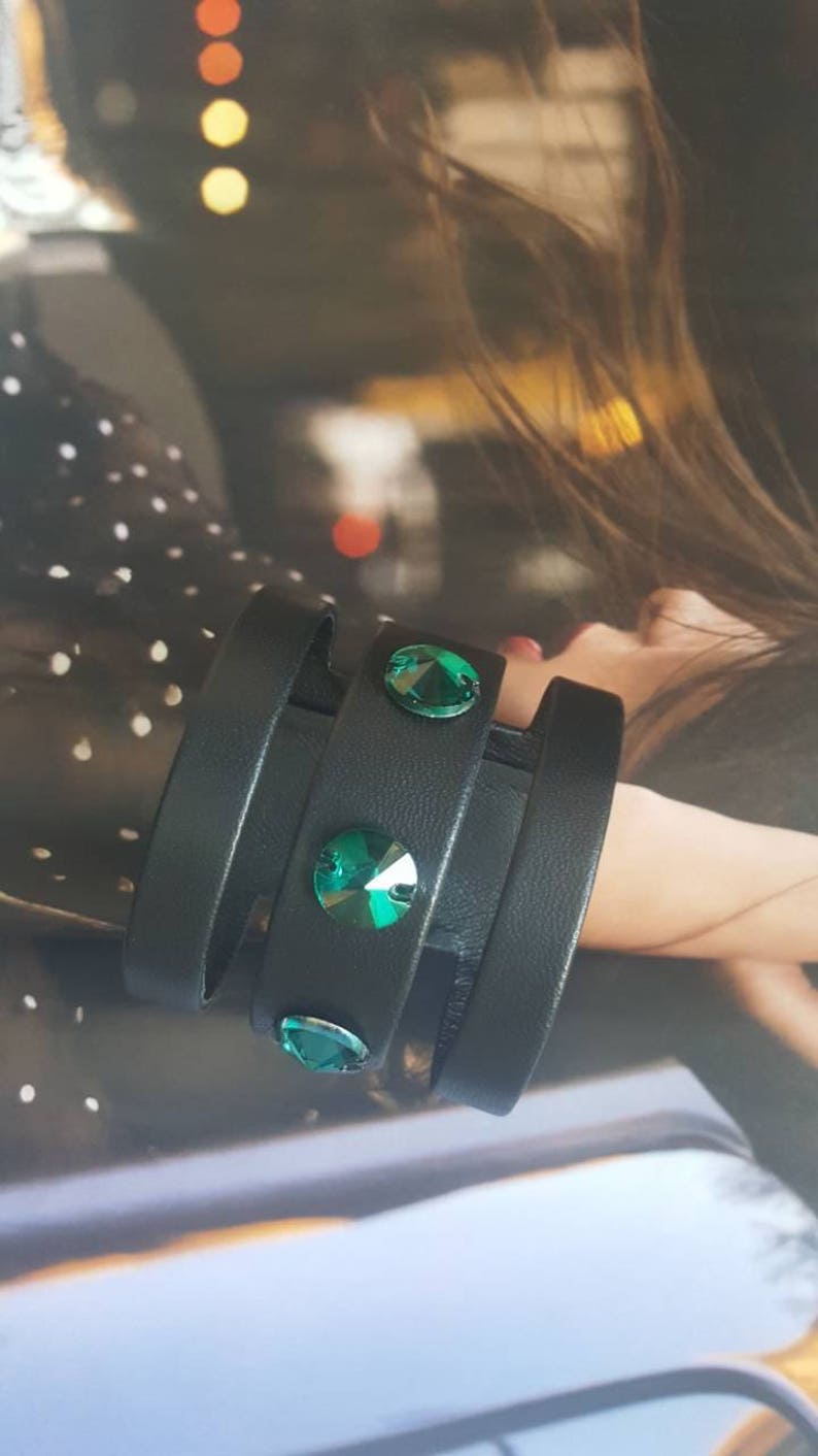 May include: A black leather bracelet with three straps and three green crystal embellishments.