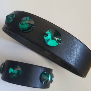 Puede incluir: Dos pulseras de cuero negro con piedras de cristal verde esmeralda. La pulsera más grande es más ancha que la más pequeña.