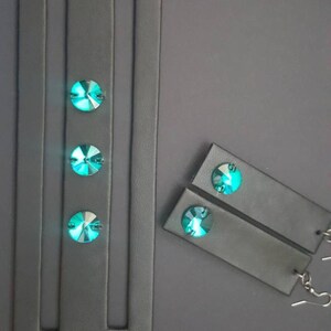 May include: A black leather bracelet with three turquoise gemstones and two black leather earrings with turquoise gemstones.