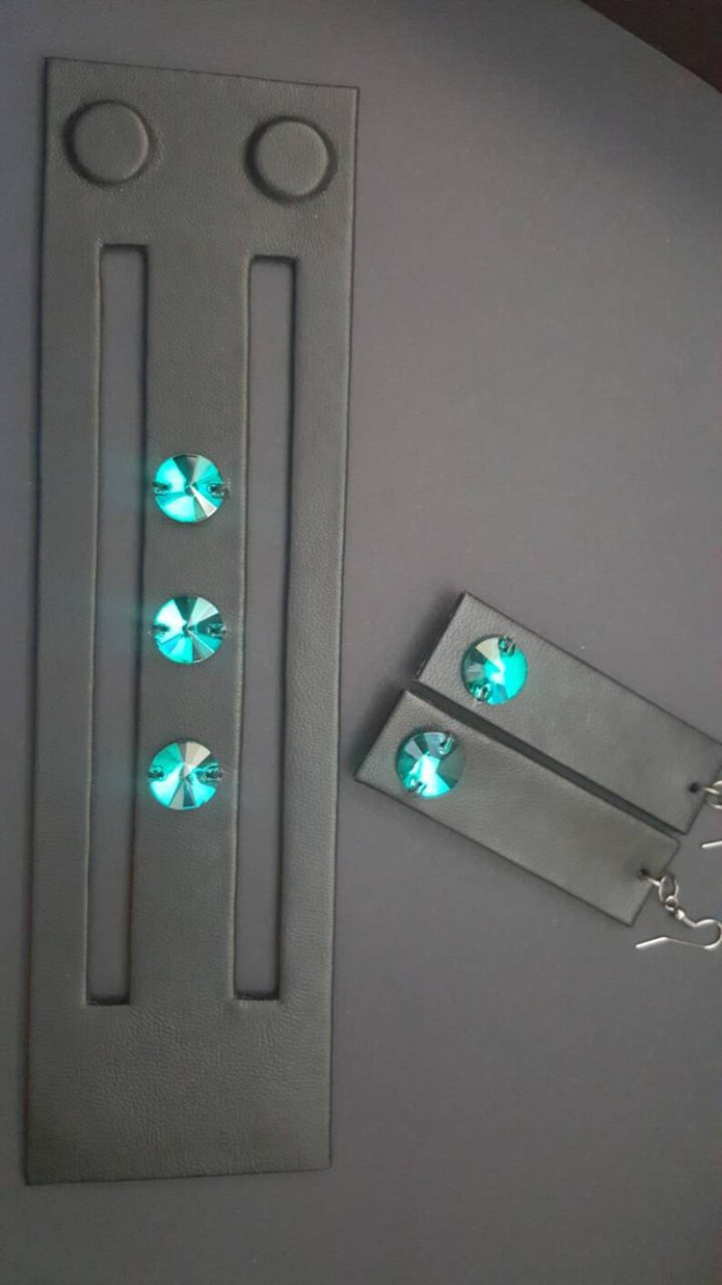 May include: A black leather bracelet with three turquoise gemstones and two black leather earrings with turquoise gemstones.