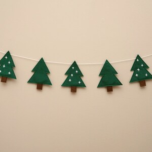 May include: A green felt Christmas tree garland with white stars. The garland is strung on a white string and has eight trees.