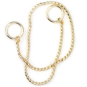 May include: A gold chain with two attached rings. The chain is braided and has a shiny finish.
