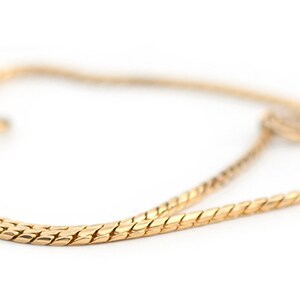 May include: A gold chain necklace with a delicate, braided design. The chain is made of a smooth, shiny metal and has a simple, elegant style.