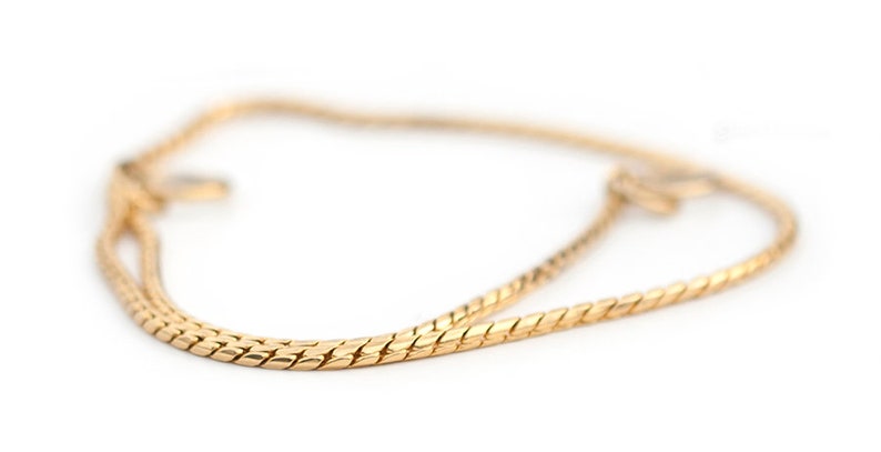 May include: A gold chain necklace with a delicate, braided design. The chain is made of a smooth, shiny metal and has a simple, elegant style.