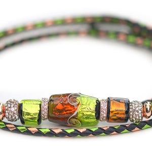 May include: A braided cord bracelet featuring a central arrangement of glass beads in shades of lime green, amber, and brown, accented by small metallic spacers and clear crystals, set against a black and metallic green woven cord base.