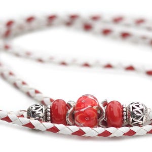 May include: A white and red braided leather cord with silver beads and a red glass bead.