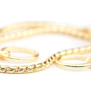 May include: A gold chain necklace with a twisted rope design and two circular clasps.