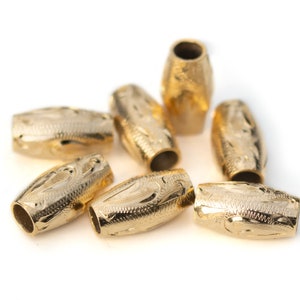 May include: Eight gold-coloured metal beads with an ornate design. The beads are oval-shaped and have a smooth, polished finish.