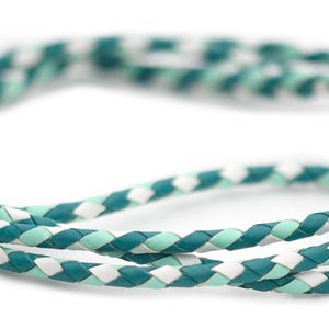 May include: A braided cord made of teal, light green, and white leather. The cord is twisted and looped, creating a decorative pattern.