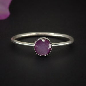 May include: A silver ring with a round, faceted, purple gemstone.