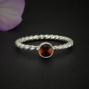 May include: A silver ring with a twisted band and a round, orange gemstone.