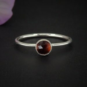 May include: A silver ring with a round, faceted, dark red gemstone.