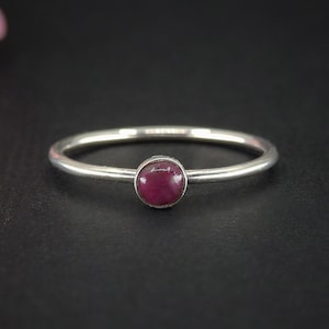 May include: A simple silver ring with a single, round, cabochon-cut, deep pink gemstone.