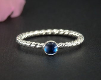 Könnte beinhalten: Ein silberner Ring mit einem gedrehten Band und einem blauen Edelstein.