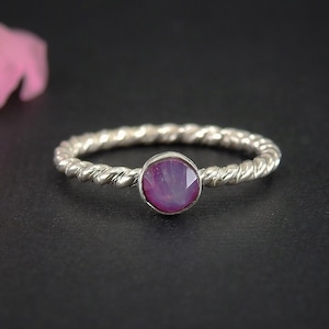 Op de afbeelding: Een zilveren ring met een gedraaide band en een roze edelsteen in het midden.