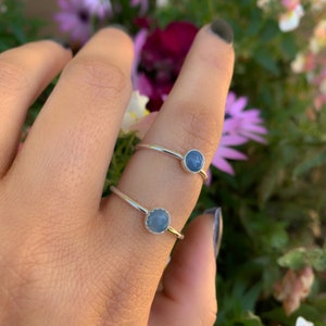 May include: Two silver rings with blue gemstone settings. The rings are on a finger.