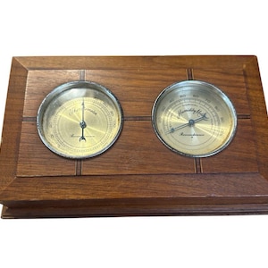 May include: A vintage wooden weather station featuring a thermometer and a humidity gauge. The gauges have gold-colored faces with black markings and silver rims. The wooden frame is a warm brown color.