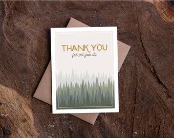 Könnte beinhalten: Dankeskarte mit einer Illustration einer Waldszene. Auf der Karte steht in goldener Schrift "THANK YOU for all you do". Sie liegt auf einem braunen Umschlag, vor einem Hintergrund aus Holzmaserung.