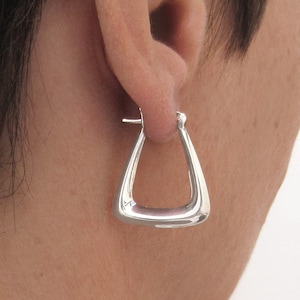 May include: Silver triangle shaped hoop earrings. The earrings are worn in a person's ear.