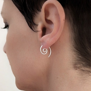 May include: A pair of silver spiral earrings. The earrings are made of thin wire that is twisted into a spiral shape. The earrings are worn in the earlobes.