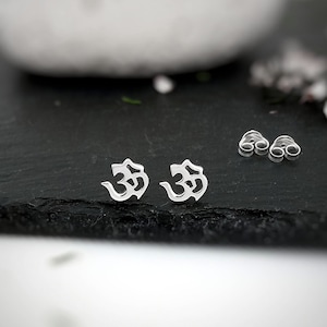 May include: A pair of silver Om symbol stud earrings. The earrings are small and delicate, and they are perfect for everyday wear.