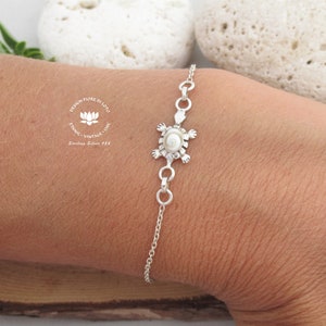 May include: A silver bracelet with a turtle pendant, featuring a central pearl. The bracelet is attached to a fine chain. The image also shows the text "DESIGN FIORE DI LOTO" and "Sterling Silver 925".