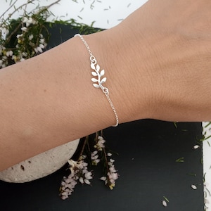 May include: A delicate silver bracelet featuring a leaf design. The bracelet is worn on a person's wrist.