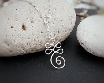 May include: A silver pendant necklace with an abstract design. The pendant has a swirling, openwork pattern suspended from a delicate chain. The necklace is displayed on a textured, light-coloured stone against a dark background.