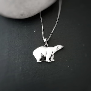 Puede incluir: Collar con colgante de oso polar plateado. El colgante es una escultura detallada en tres dimensiones de un oso polar. La cadena del collar es una fina cadena de plata. El oso mira hacia la derecha.