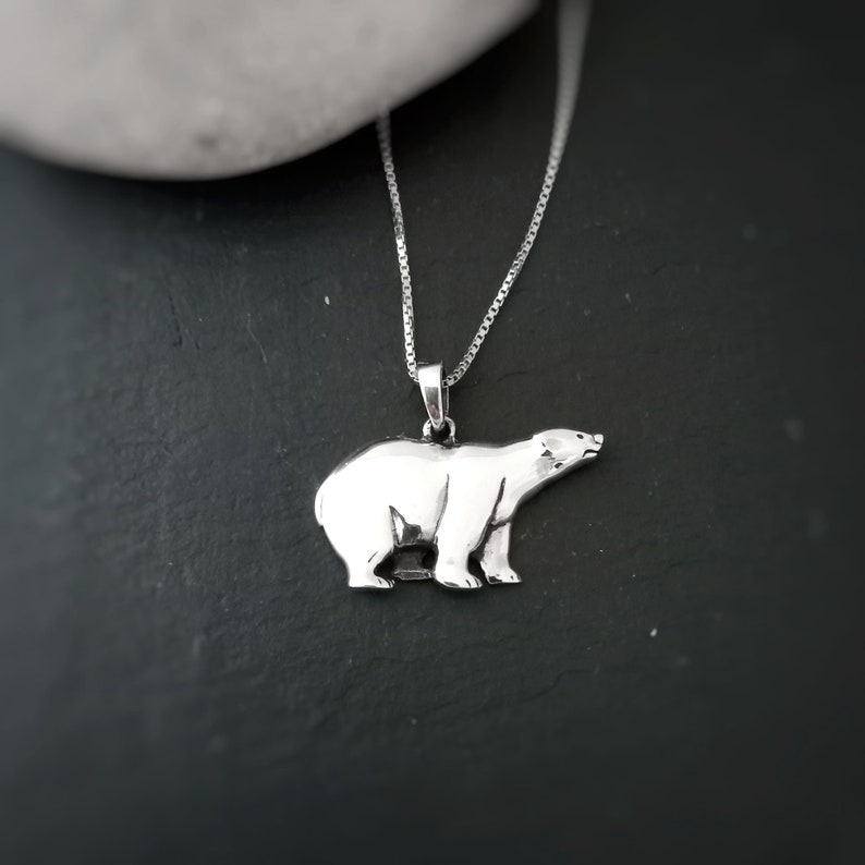 Puede incluir: Collar con colgante de oso polar plateado. El colgante es una escultura detallada en tres dimensiones de un oso polar. La cadena del collar es una fina cadena de plata. El oso mira hacia la derecha.