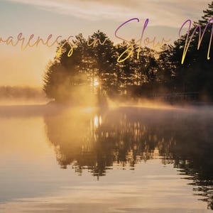 Op de afbeelding: Een serene landschap met een meer bij zonsopgang. Het water weerspiegelt de lucht en de bomen aan de horizon. De tekst "Awareness in Slow Motion" staat in gouden letters bovenaan.