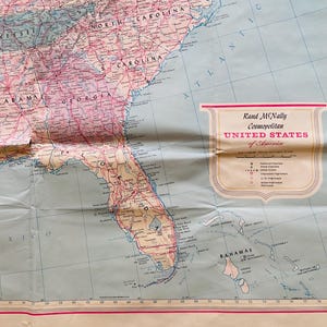 May include: A vintage map of the southeastern United States, featuring states like Florida, Georgia, and the Carolinas. The map has a pink and blue color scheme with the text "Rand McNally Cosmopolitan UNITED STATES of America".