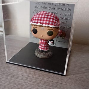 May include: A red and white checkered pop figure of a woman holding a small white penguin. The figure is in a clear display case with a black base. The text on the back of the case reads: "So, let me get this straight you want to fly a magic carpet of the land and your chin 2 hours."