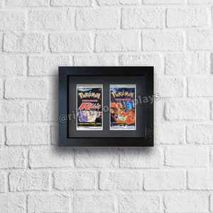 May include: Two Pokemon trading cards, one featuring a character named "Ritz" and the other featuring a red and orange Pokemon, are displayed in a black frame against a white brick wall.
