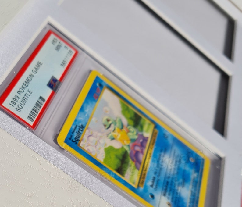 May include: A graded 1999 Pokemon Game Squirtle card in a protective case. The card features a blue background with an illustration of Squirtle, a water-type Pokemon, in a grassy field.