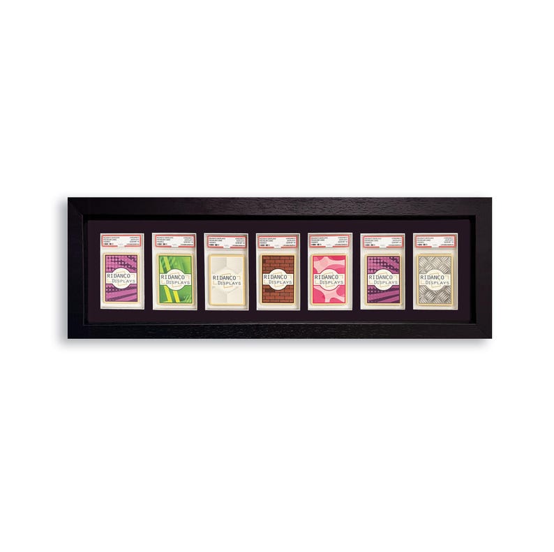May include: A black framed display case holding seven trading card holders. Each holder contains a card with a unique design and the text "REDANCO DISPLAYS". The cards have various colors, including pink, green, and brown.