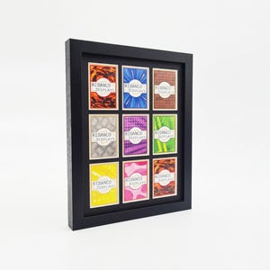 Op de afbeelding: Een zwarte rechthoekige schaduwdooslijst met negen individuele verzamelkaarten gerangschikt in een drie-bij-drie raster. Elke kaart heeft een uniek kleurrijk grafisch patroon en de tekst RIDANCO DISPLAYS gedrukt in een wit cirkelvormig logo.