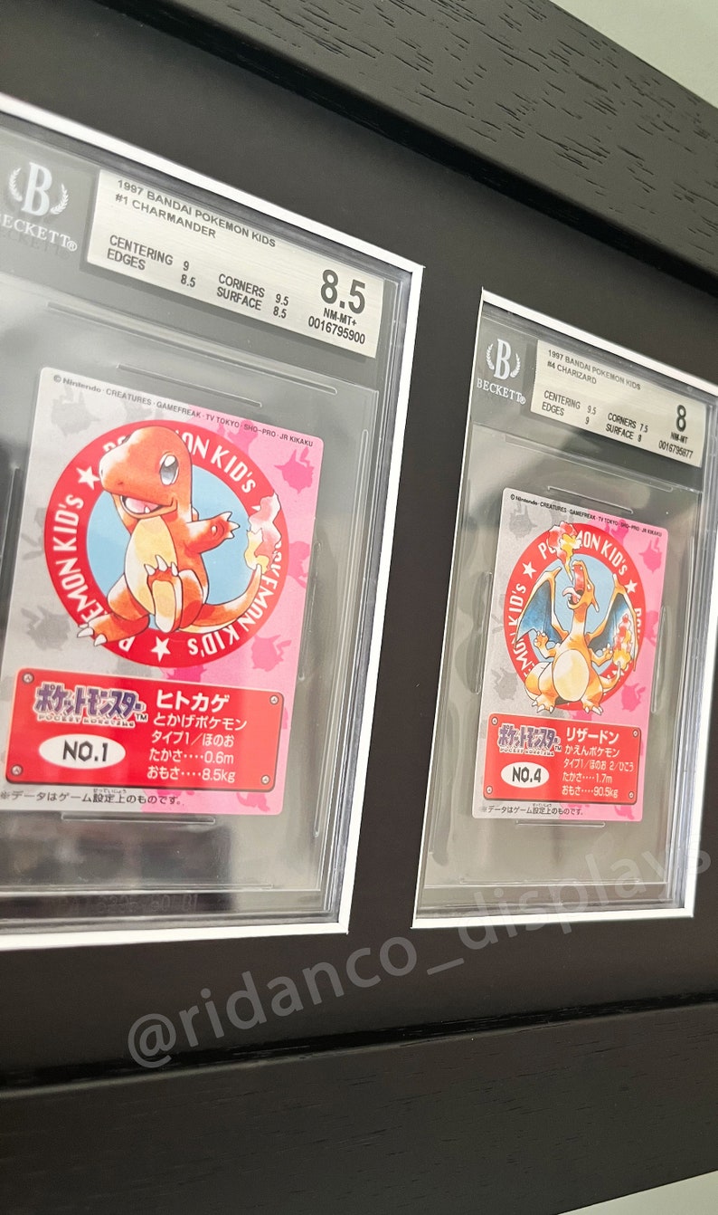 May include: Two Pokemon trading cards graded by Beckett Grading Services. The cards are both from the 1997 Bandai Pokemon Kids set. The first card is a Charmander, graded NM-MT+ 8.5. The second card is a Charizard, graded 8. Both cards feature the Pokemon in a circular frame with Japanese text.